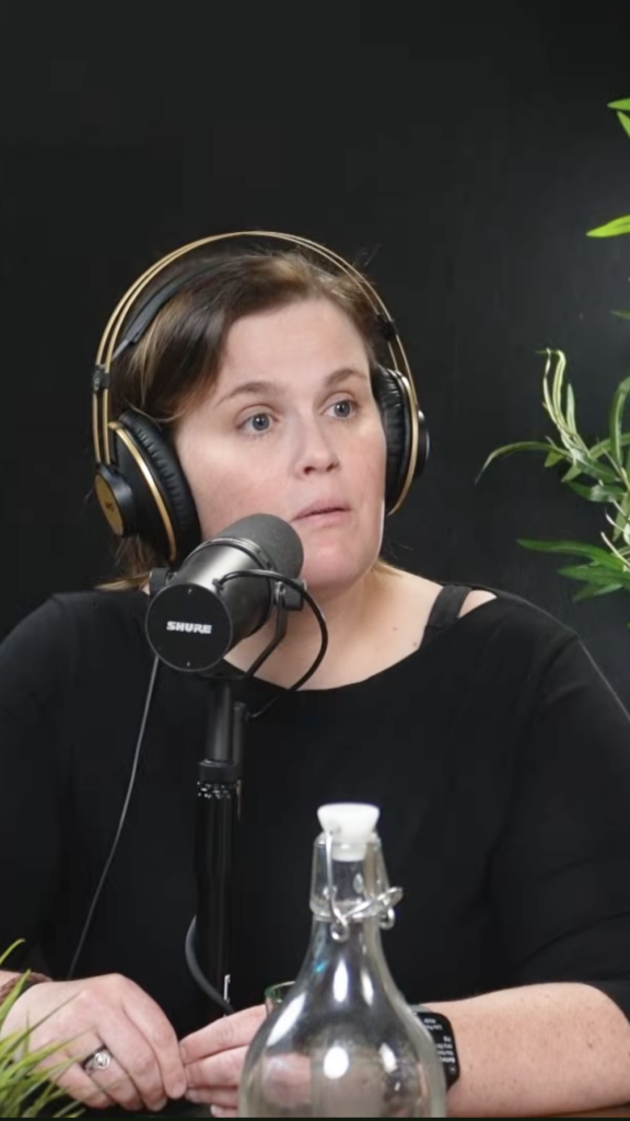 vertical image of trauma therapist and social worker Kristina Fifield. She's wearing headphones and speaking into a mic during recording of the podcast